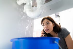 Leak under sink, woman on the phone calling repair service.