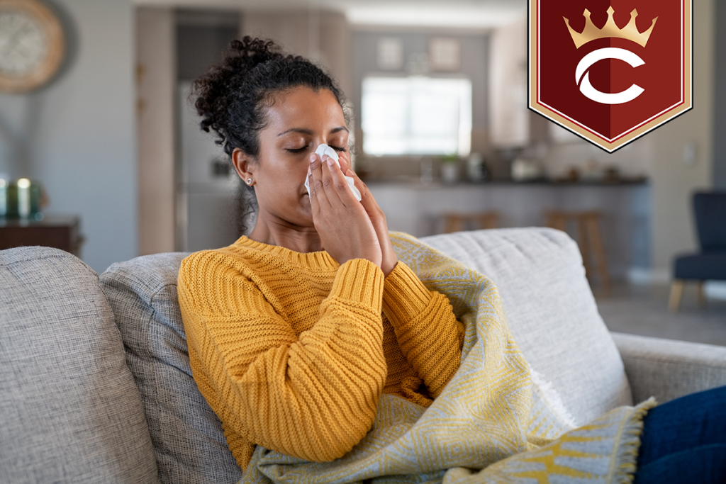 A woman in a yellow sweater on her sofa blowing her nose into a tissue